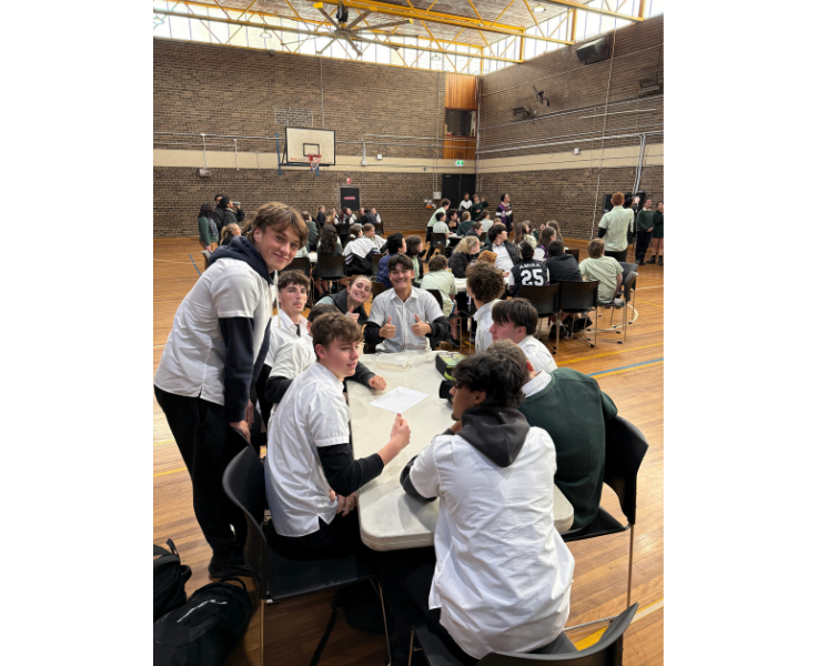 Students and teachers sitting at tables participating in the Trivia Quizz